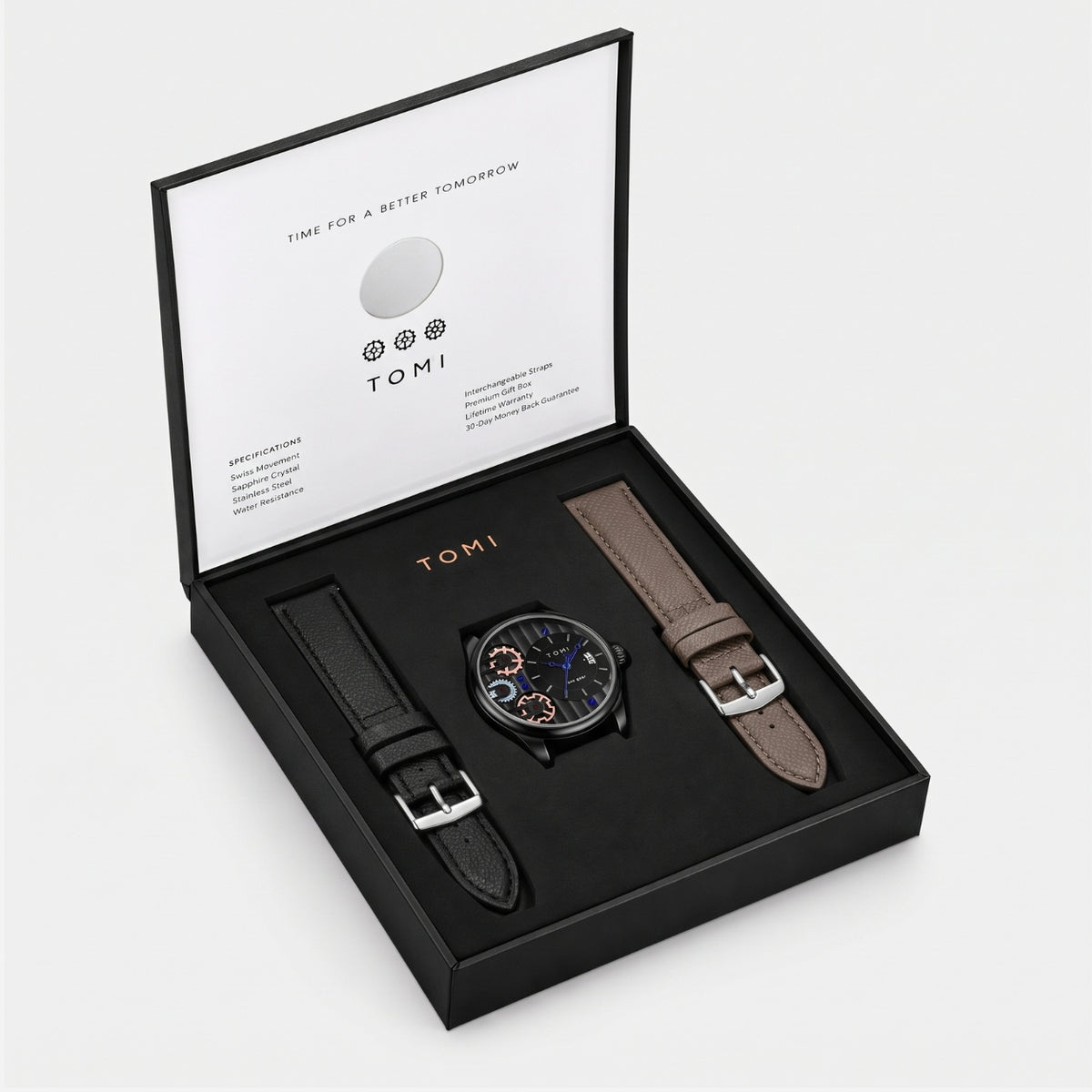 A TOMI watch gift set in an open black presentation box on a light gray background. The set includes a round analog watch with a dark dial, a black leather strap, a brown leather strap, and branded box packaging with the TOMI name visible on the interior lid.
