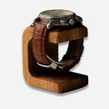 Watch with brown leather strap on a wooden stand against a white background