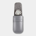 A silver leather watch pouch holding a silver-toned watch with a white dial, shown against a light gray background.