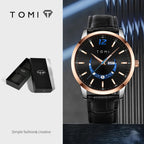 TOMI watch with black leather strap and black face on a dark background, next to TOMI packaging.