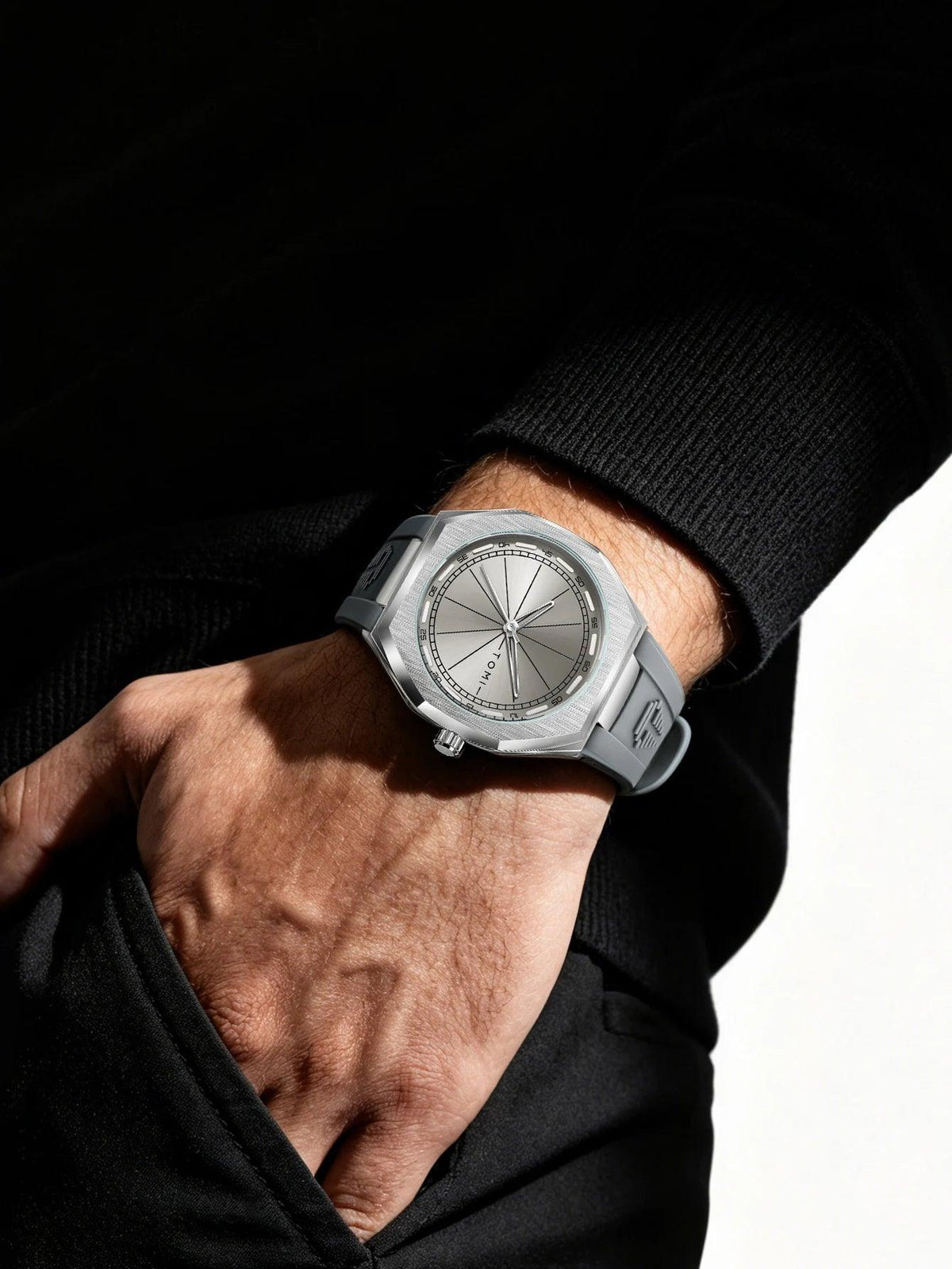 A close-up of a person's hand and wrist wearing a silver-toned watch with a matte gray dial and matching gray strap, styled with a black knit sweater against a dark background.