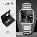 Silver watch with black dial and gift box on a gray background, featuring the TOMI brand.
