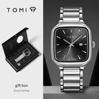Silver watch with black dial and gift box on a gray background, featuring the TOMI brand.