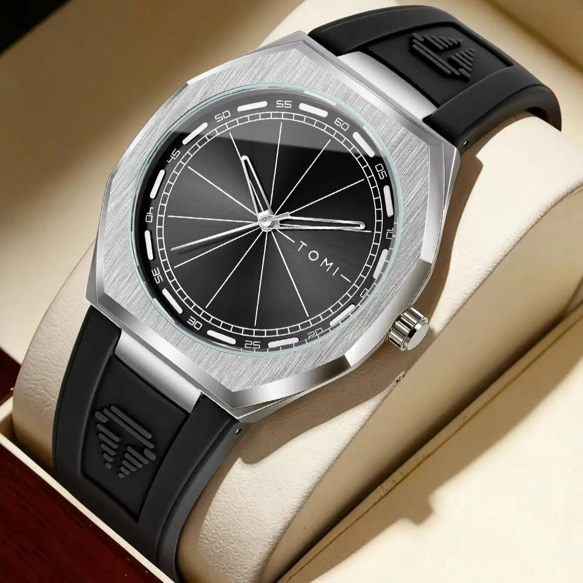 A close-up of a wristwatch with a brushed silver-tone case, black dial, and black rubber strap, resting on a cream-colored display cushion inside a watch box.