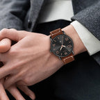 Person wearing a watch with a brown leather strap and black dial.