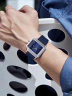 Person wearing a blue watch with a geometric face on a blurred background