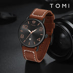 Brown leather watch with black dial on a dark background, featuring the brand 'TOMI'.