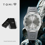 TOMI stainless steel watch with a brushed silver dial and matching gray silicone strap, shown alongside its black presentation box on a split white and dark background.
