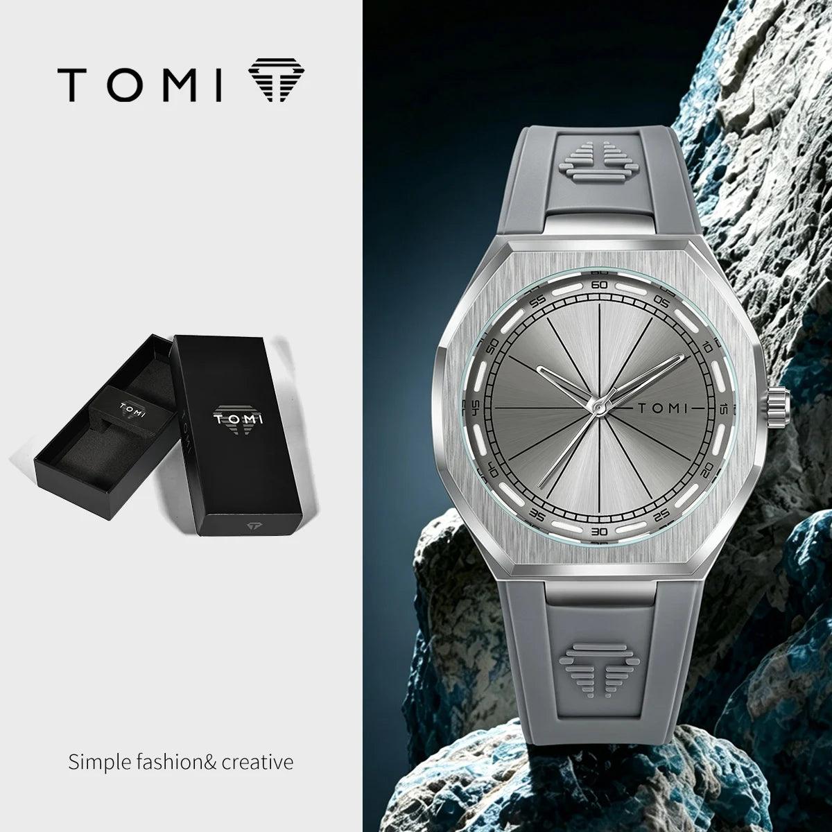 TOMI stainless steel watch with a brushed silver dial and matching gray silicone strap, shown alongside its black presentation box on a split white and dark background.