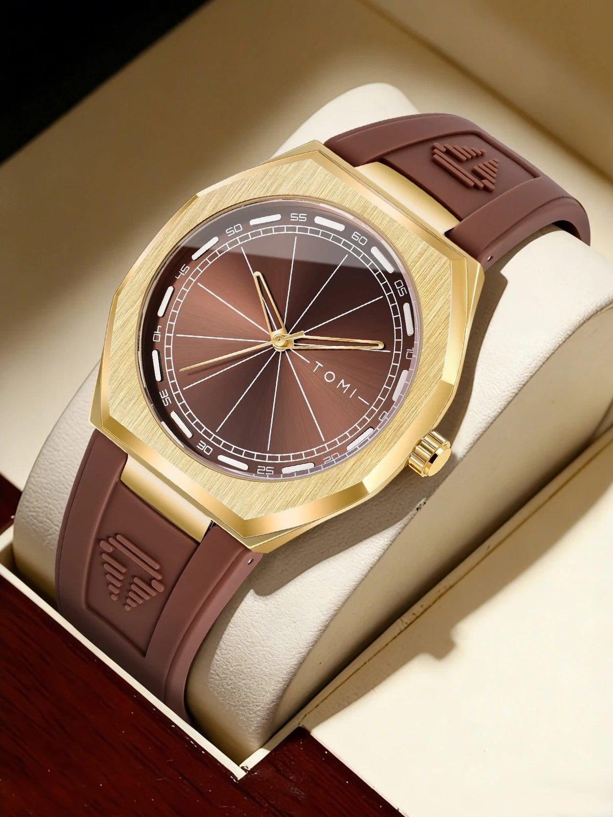 A luxury wristwatch with a brushed gold-tone octagonal case, a brown sunburst dial, and a matching brown rubber strap, presented inside a cream-colored watch box.
