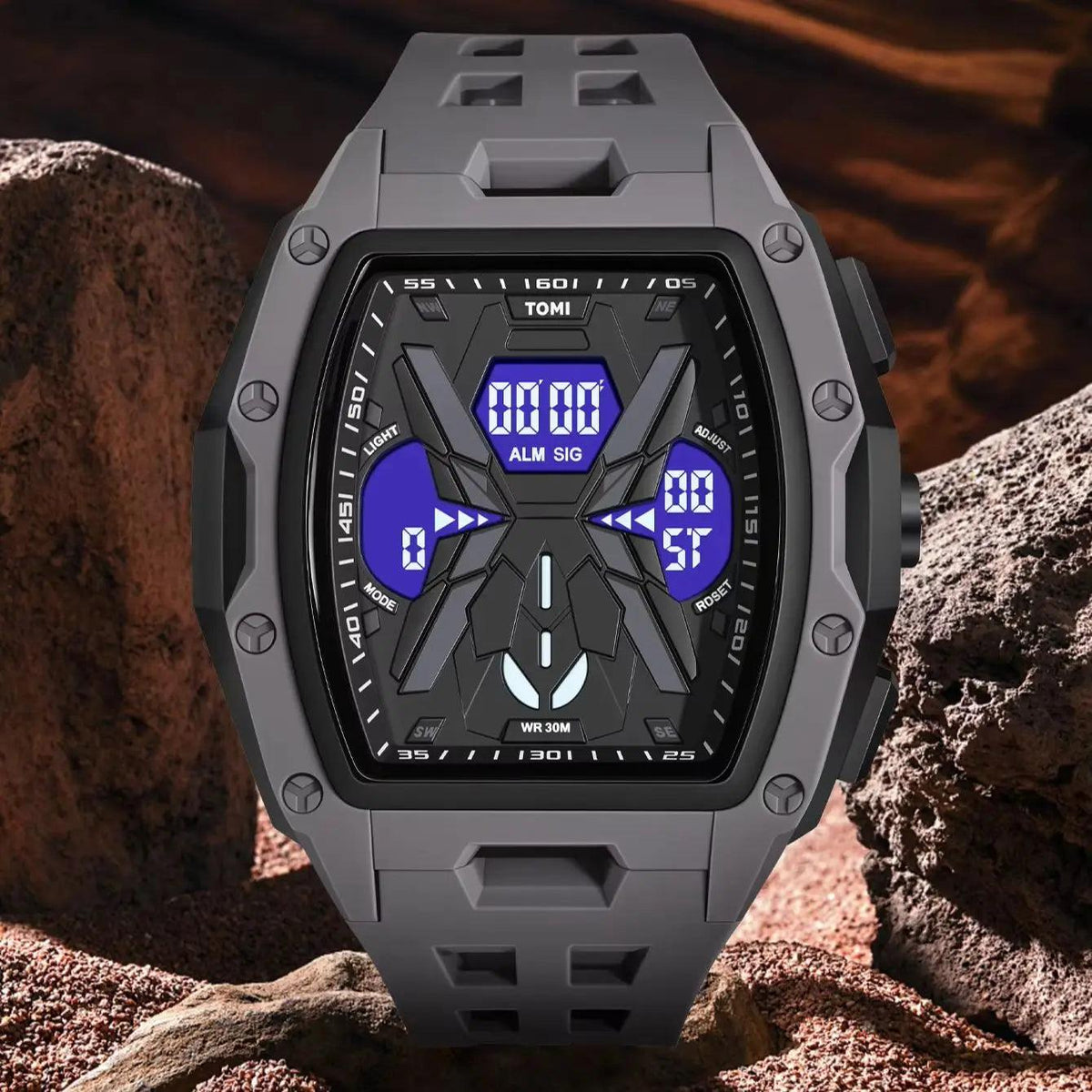 A rugged digital watch with a dark gray and black case and strap, featuring a blue display screen, set against a rocky desert background.