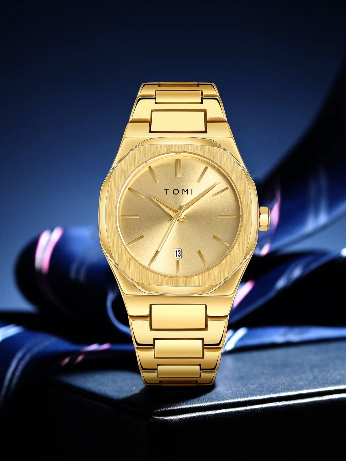A gold-tone stainless steel wrist watch with a matching metal link bracelet, featuring a brushed dial, slim stick indices, and a date window at the 3 o'clock position. The brand name 'TOMI' is printed on the dial.