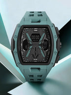 A rugged digital watch with a matte teal-green case and strap, black dial, and silver screw details, shown on a stylized light blue and black geometric background. The brand name TOMI is visible on the watch face.