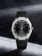 A TOMI watch with a brushed silver-tone octagonal case, black dial, and black rubber strap, photographed against a dark textured studio background.
