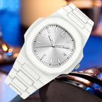 A white analog watch with a matching white silicone or rubber strap, featuring a silver-toned dial, silver hour markers, and a silver crown, shown against a blurred blue and brown background.