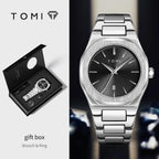 Tomi brooch and ring watch gift set shown with the open black presentation box on the left and the silver-toned metal watch on the right. The watch has an octagonal silver case, a brushed silver bracelet, and a dark charcoal dial with silver indices.