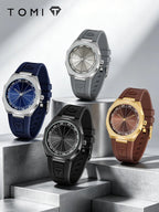 Four TOMI watches displayed on metallic pedestal steps: navy blue, gray, black, and gold-tone with brown, blue, gray, and rose-gold dials. The TOMI logo appears in the top left.