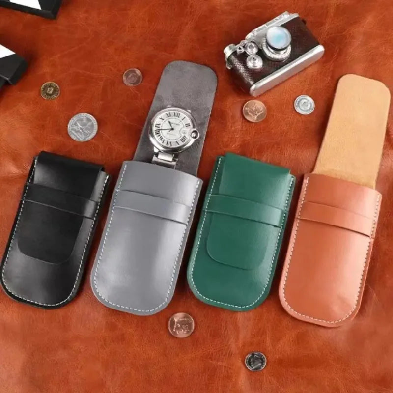 Set of leather pouches in black, gray, green, and brown on a brown leather surface with coins and a camera.