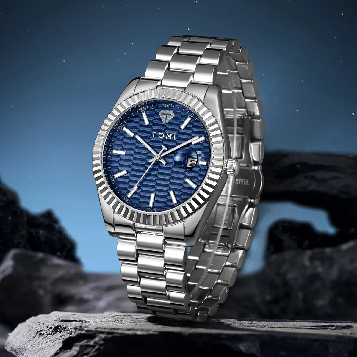 Silver watch with blue dial on a rocky surface at night