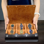 Open brown watch case with five watches displayed on a wooden surface.