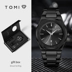 Tomi black watch gift set featuring a black metal bracelet watch with a brushed black dial, shown alongside its open black presentation box containing the watch and two rings.
