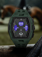 A rugged digital watch with an olive green silicone strap and a black textured case, featuring a blue and black display. The watch is shown resting on a dark wooden surface with a blurred outdoor background containing horses.