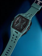 A rugged digital watch with a matte teal-green strap and case, black face, and silver buckle, shown diagonally on a dark blue gradient background.