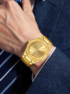 A gold-tone metal watch with an octagonal bezel and matching link bracelet, worn on a wrist. The watch features a gold dial with slim hour markers and a small blue logo accent.