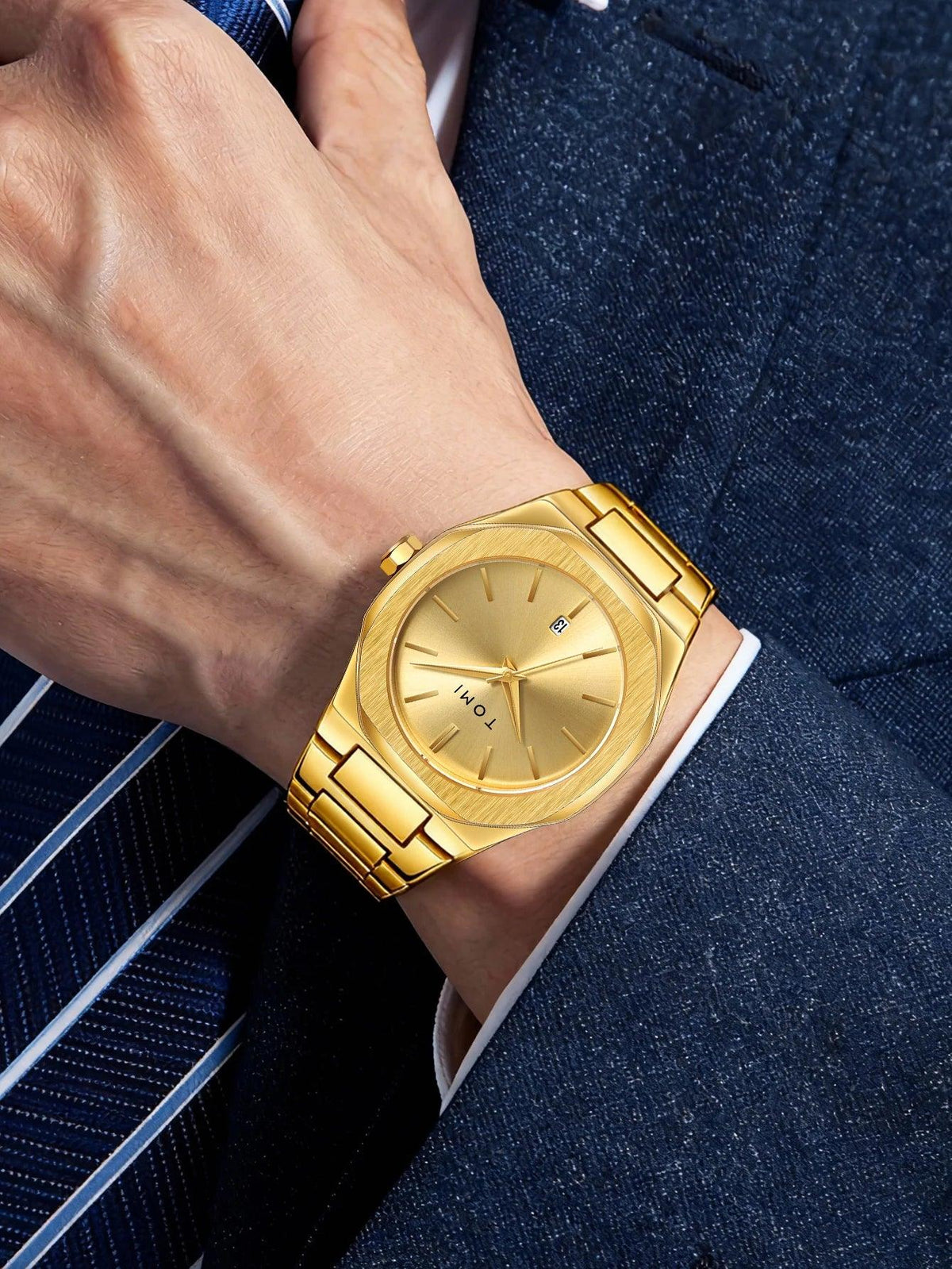 A gold-tone metal watch with an octagonal bezel and matching link bracelet, worn on a wrist. The watch features a gold dial with slim hour markers and a small blue logo accent.