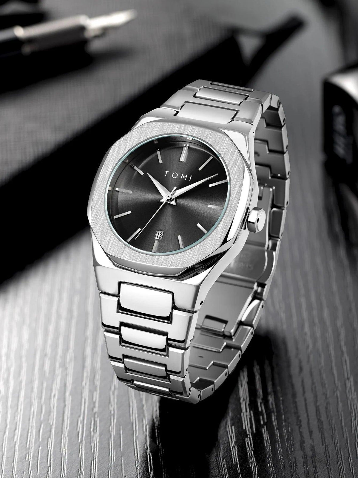 Silver watch with black face on a reflective surface