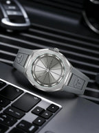 A silver-toned Tommi watch with a brushed metal case and strap, resting on a laptop keyboard with a blurred car key fob in the background.