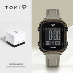Digital watch with gray strap and black display, featuring the TOMI brand, on a light beige background.