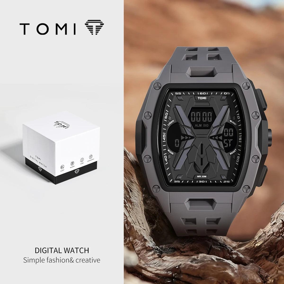 A TOMI digital watch with a rugged dark gray and black case and face, displayed next to its white branded box on a split background. The watch is shown on a piece of wood in an outdoor setting, while the box is photographed on a clean white background.