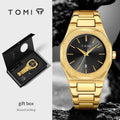 TOMI men's watch shown in a split layout: on the right, a gold-tone brooch-style link bracelet watch with a brushed gold case and black dial is displayed against a dark rock background; on the left, the watch is shown open in a black gift box with the TOMI logo and text reading 'gift box' and 'Brooch & Ring'.