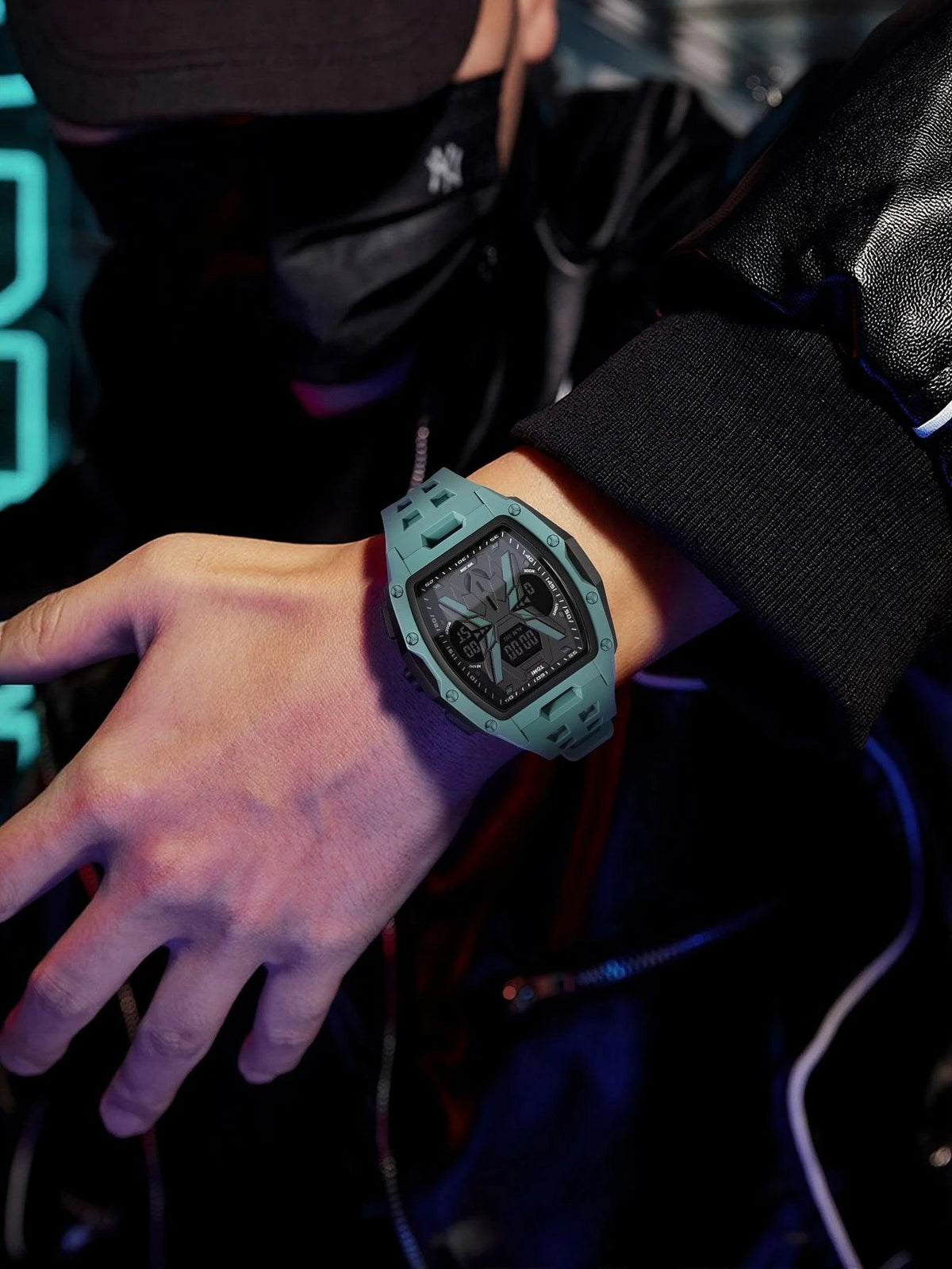 A rugged Casio watch with a teal-green and black case worn on a person's wrist, shown in a dark, urban setting with neon lighting.