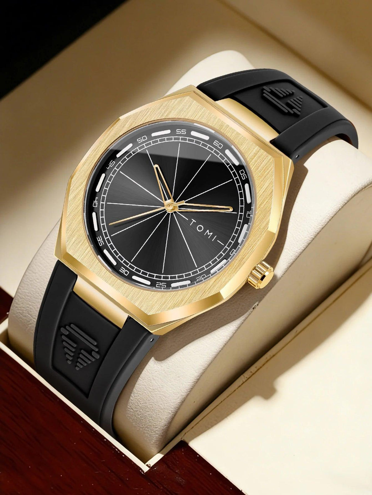A luxury wristwatch by TOMI, featuring a brushed gold-tone case, a black dial with gold hands and markers, and a black rubber strap with a gold buckle, presented inside its cream-colored box.