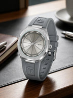 A silver and gray Tomi watch with a brushed metal case and a gray silicone strap, resting on a dark desk mat over a wooden surface.