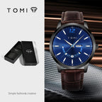 TOMI watch with blue dial and brown leather strap, displayed with packaging on a dark background.