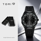 Tomi black analog watch with a textured dial and matching black strap, shown alongside its open presentation box on a clean light gray background.
