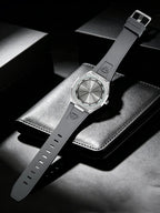 A wristwatch with a dark gray strap and a silver-toned octagonal case, displayed diagonally on a textured black leather surface with dark background boxes.