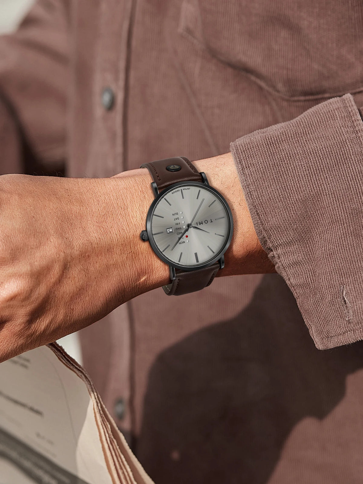 Person wearing a watch with a brown leather strap on a blurred background