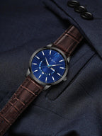 Watch with a blue face and brown leather strap on a dark suit background