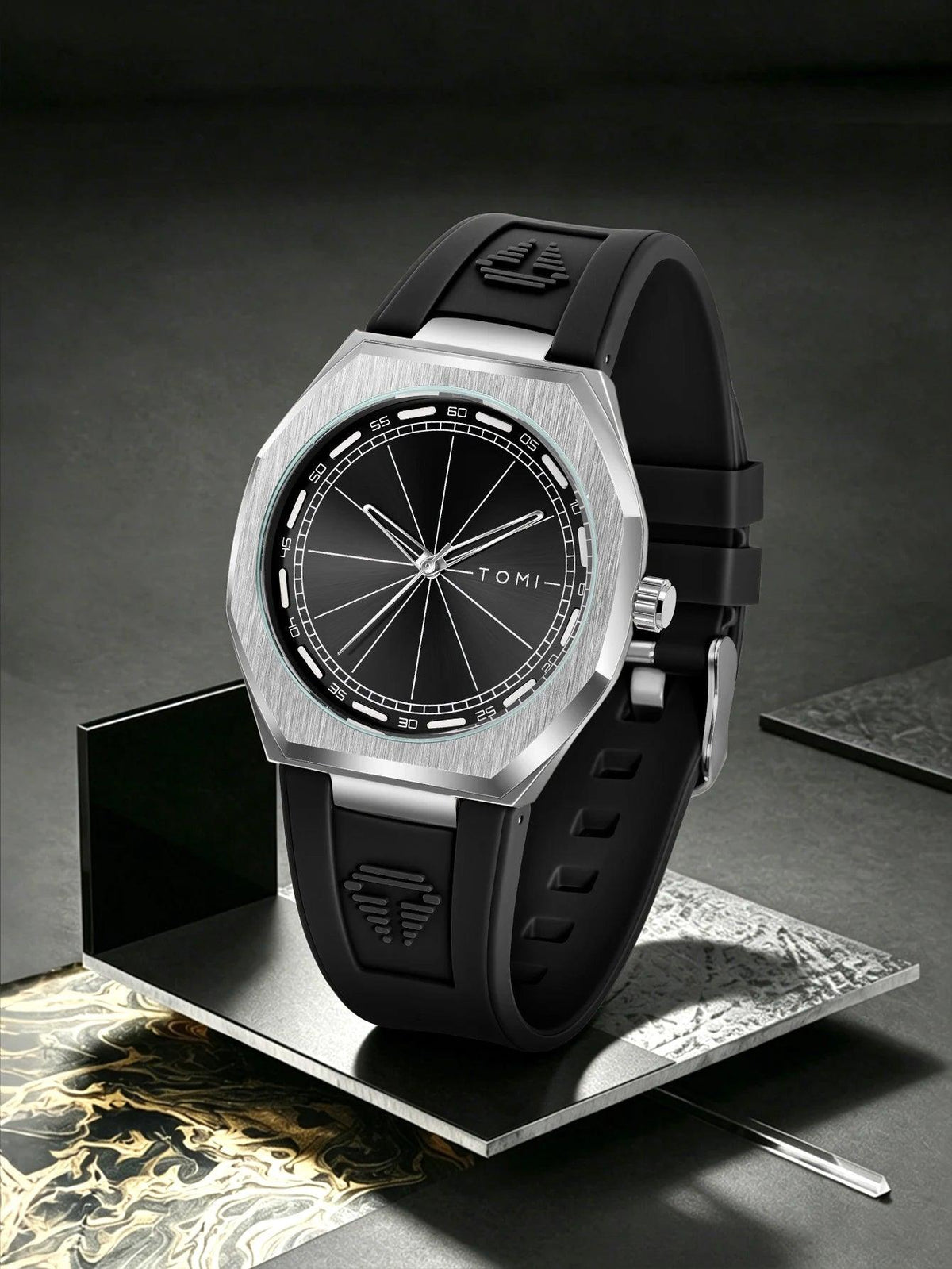 A Tomi watch with a brushed silver octagonal case, black dial, and black rubber strap, displayed on a metallic stand against a dark gray background.
