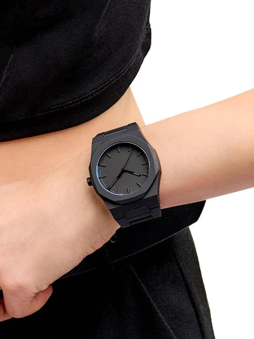 Black wristwatch on a person's wrist with a plain background