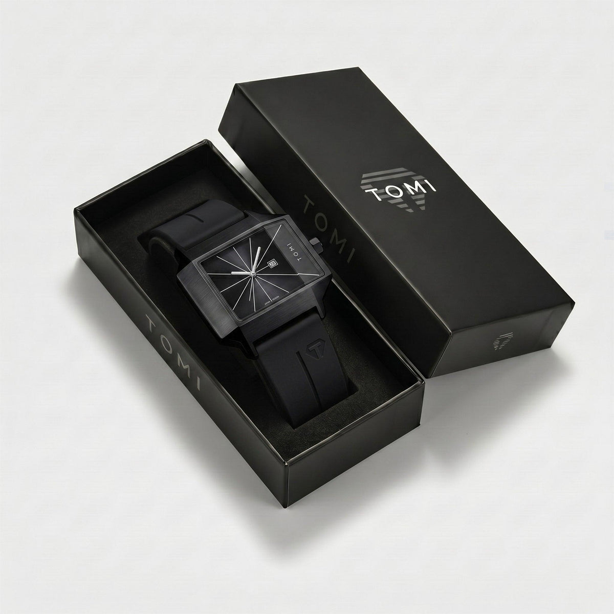 Black watch in an open black box with 'TOMI' branding on a light gray background